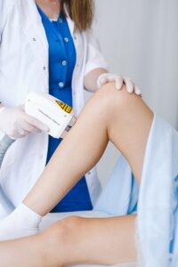 Médecin méconnaissable en uniforme médical et gants utilisant un équipement professionnel pour une thérapie au laser de faible intensité pour un client