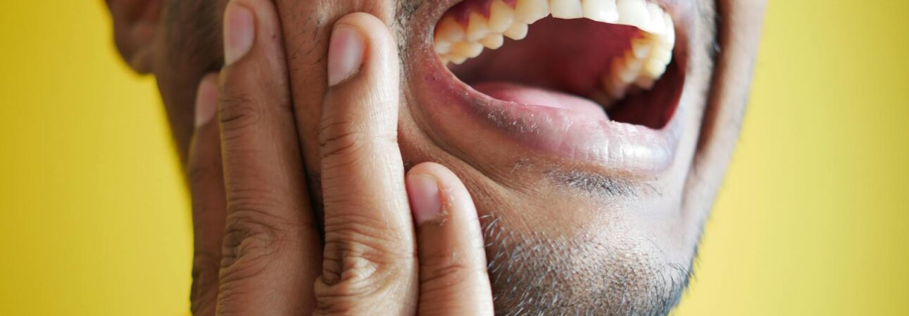 Gros plan d'un homme se tenant la joue, affichant une bouche grande ouverte sur un fond jaune.