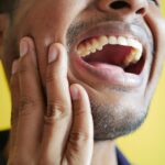 Gros plan d'un homme se tenant la joue, affichant une bouche grande ouverte sur un fond jaune.