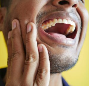 Gros plan d'un homme se tenant la joue, affichant une bouche grande ouverte sur un fond jaune.