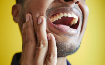 Gros plan d'un homme se tenant la joue, affichant une bouche grande ouverte sur un fond jaune.