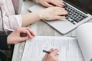 Gros plan de mains tapant sur un ordinateur portable et examinant des documents commerciaux, concentrés sur des tâches financières et juridiques.